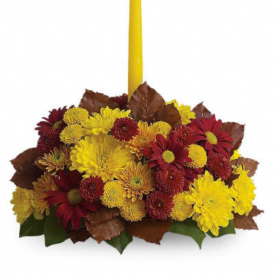 Yellow taper candle in a low arrangement of red and yellow chrysanthemums