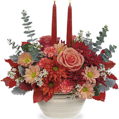 Red and peach floral arrangement with two red taper candles in a white bowl vase