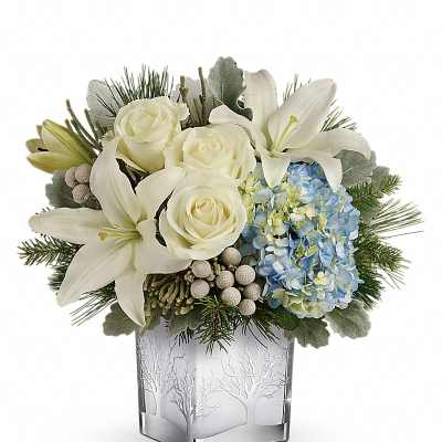 White lilies and roses arranged with blue hydrangea in a frosted glass vase