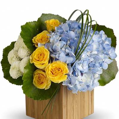 Yellow roses and blue hydrangeas in a wooden cube vase
