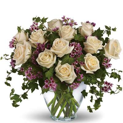 Cream roses and purple filler flowers in a clear glass vase