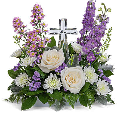 White roses and purple flowers arranged around a clear glass cross