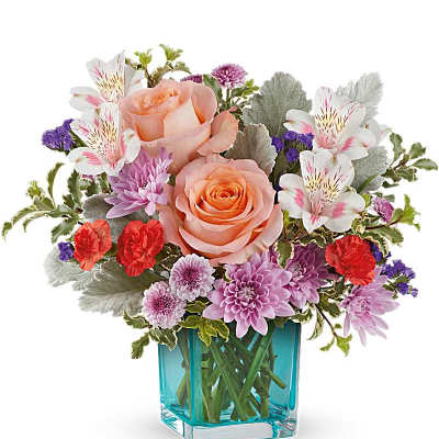 Mixed bouquet of peach roses, purple flowers, and white alstroemeria in a blue glass vase