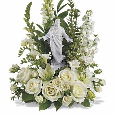 White roses and lilies arranged around a small white religious statue