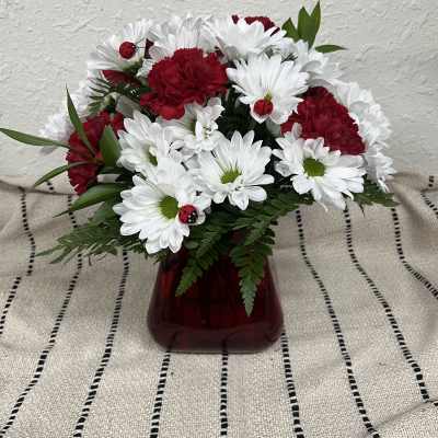 Red carnations and white daisies in a red vase with small ladybug decorations