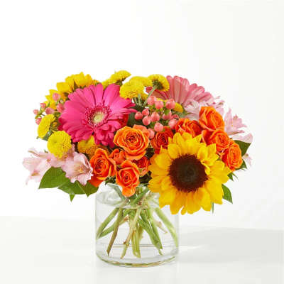 Bright bouquet of sunflowers, pink gerbera daisies, and orange roses in a clear glass vase