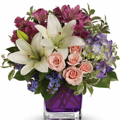 Bouquet of white lilies, pink roses, and purple flowers in a purple glass vase