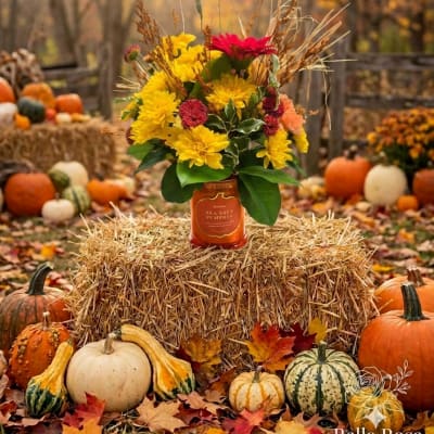 Fall flower arrangement in a candle jar surrounded by pumpkins and hay bales