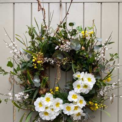 Spring wreath with white and yellow flowers and wild branches on a light gray paneled door