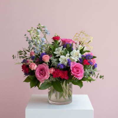 Mixed pink and white flowers in a glass vase with a birthday topper