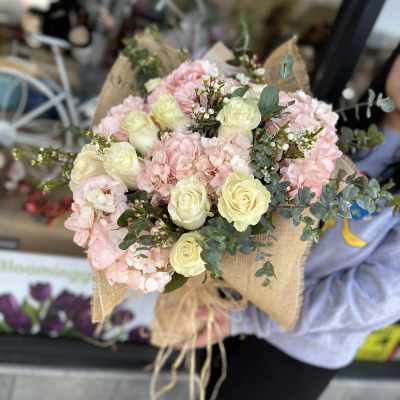 Bouquet of pale pink hydrangeas and cream roses wrapped in burlap