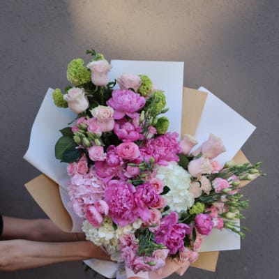 Handheld bouquet of pink and white flowers wrapped in paper
