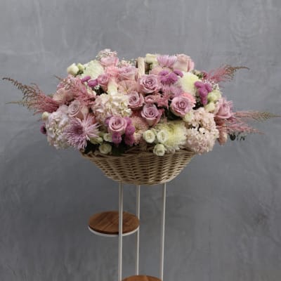 Large pink and white floral arrangement in a wicker basket on a stand