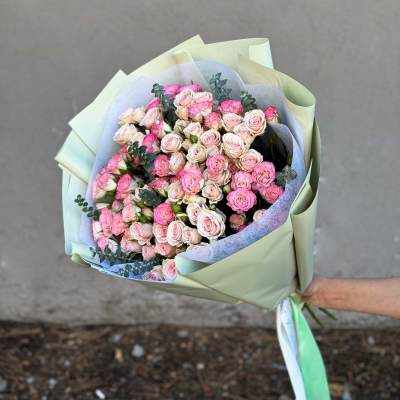 Hand-tied bouquet of pink and blush roses wrapped in pale green paper
