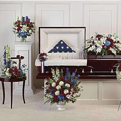 Funeral casket surrounded by patriotic red, white, and blue floral sprays