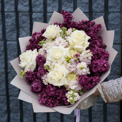 Bouquet of white roses and purple lilacs wrapped in pale paper