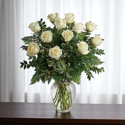White roses arranged in a clear glass vase with greenery