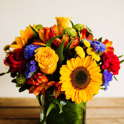 Colorful bouquet in a square glass vase with a sunflower and roses
