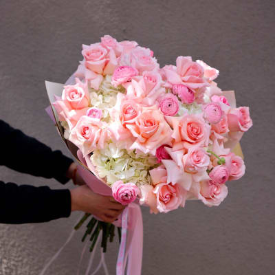 Handheld bouquet of pink roses and pale flowers wrapped with pink ribbon
