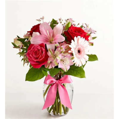 Bouquet of red roses, pink lilies, and a white gerbera daisy in a glass vase