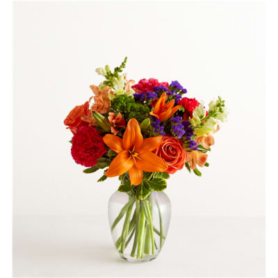 Bright mixed bouquet with orange lilies and roses in a clear glass vase
