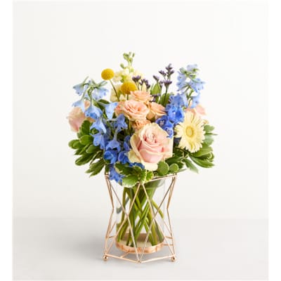 Mixed bouquet of pink roses, blue flowers, and yellow blooms in a glass vase