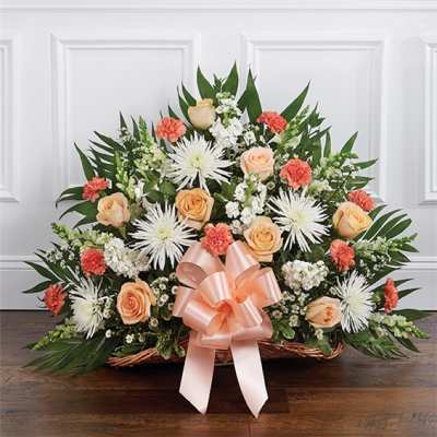 Basket arrangement of peach roses, white spider mums, and coral carnations with a pink bow