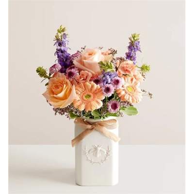 Peach roses and purple flowers in a white vase with a ribbon