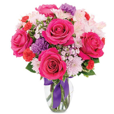 Pink roses and mixed flowers in a clear glass vase with a purple ribbon