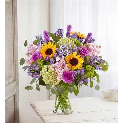 Mixed bouquet with sunflowers, purple blooms, and pink flowers in a glass vase
