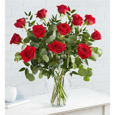 Red roses in a clear glass vase with green foliage