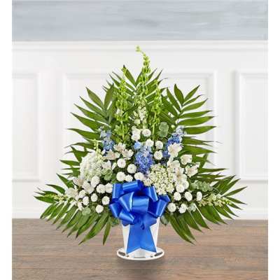 Standing floral arrangement with white and blue flowers and a blue ribbon in a white container
