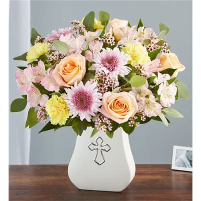 Pastel mixed flower arrangement in a white vase with a cross emblem