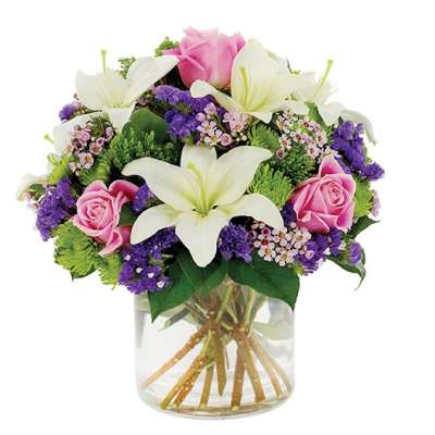 Bouquet of white lilies, pink roses, and purple filler flowers in a glass vase