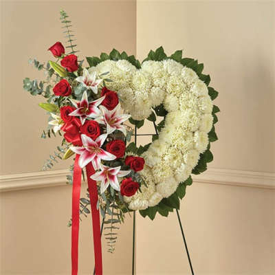 Heart-shaped floral wreath with red roses and white lilies on a stand