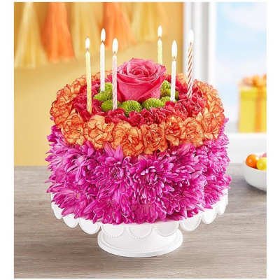 Round floral cake arrangement with a pink rose and lit candles on a white pedestal stand