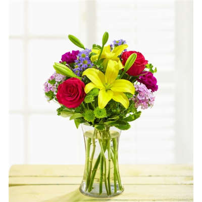 Bouquet of yellow lilies, red roses, and purple flowers in a clear glass vase