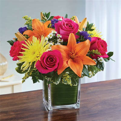 Bright mixed bouquet in a square glass vase with roses, lilies, and mums