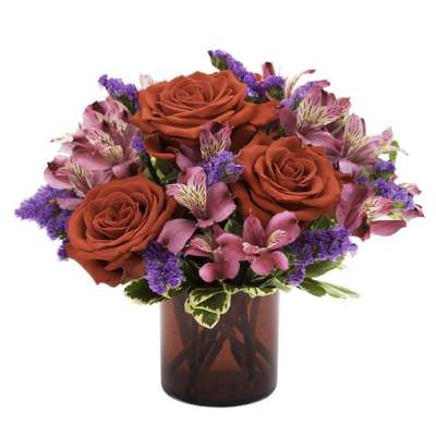 Red roses and pink flowers arranged in a red glass vase