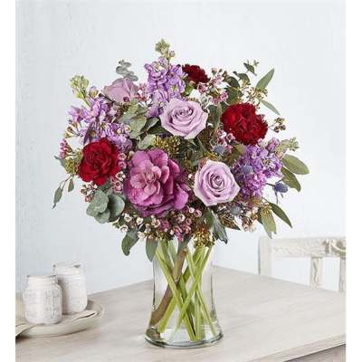 Mixed bouquet of roses and purple flowers in a clear glass vase