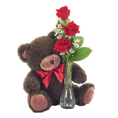 Teddy bear beside a glass vase with red roses and small white flowers