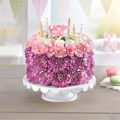 Pink and purple flower cake with striped candles on a white stand