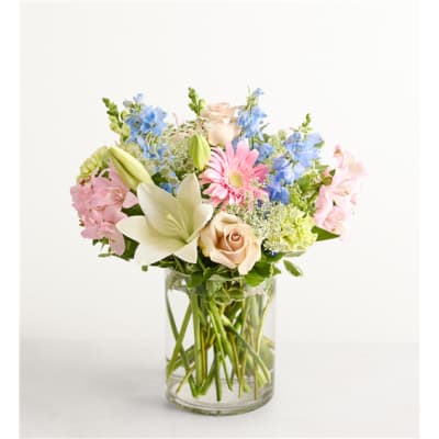 Mixed pastel bouquet in a clear glass vase with roses, lilies, and blue flowers