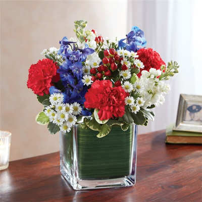 Mixed bouquet of red, blue, and white flowers in a square glass vase