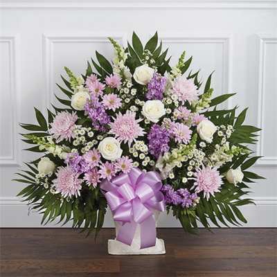 Lavender and white floral arrangement in a white container with a purple bow