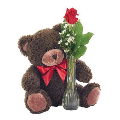 Teddy bear beside a glass vase with red roses and small white flowers
