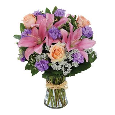 Pink lilies and roses in a glass vase with purple accents