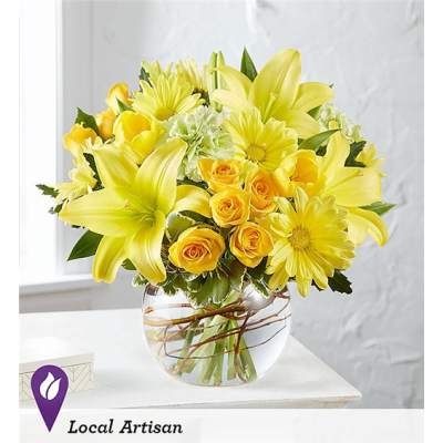 Yellow lilies and roses arranged in a clear glass vase