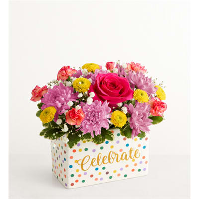 Pink and yellow mixed flower arrangement in a polka-dot box with "Celebrate" text