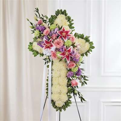 Standing floral cross with pink lilies, roses, and white blooms on an easel